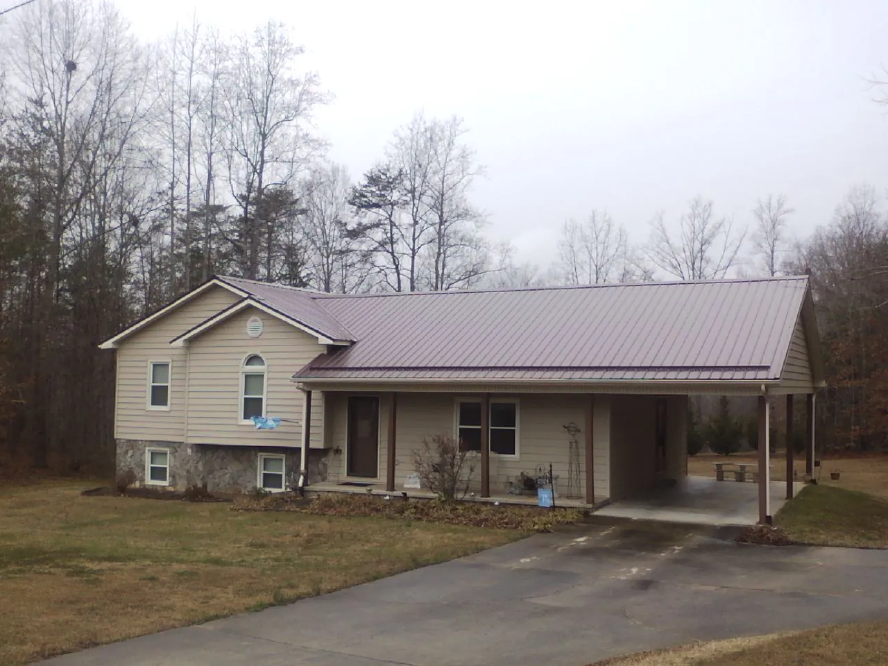 Burgundy metal roof on a tan split level home with an attached carport in Denton