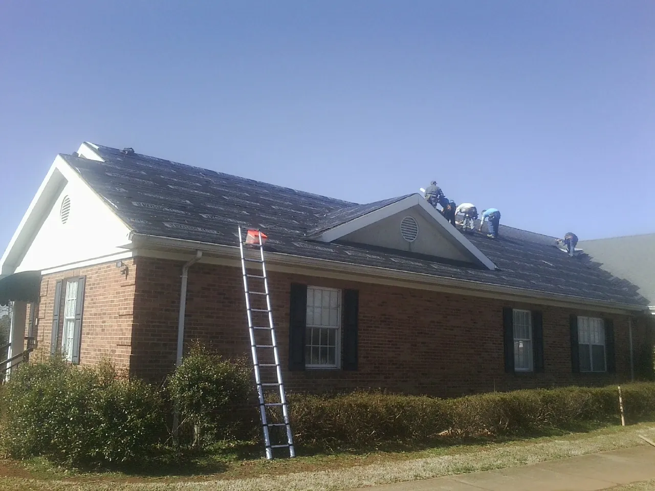 Crew tearing shingles off a brick ranch roof with a ladder set — Metal Roof Repair work by our crew in Denton